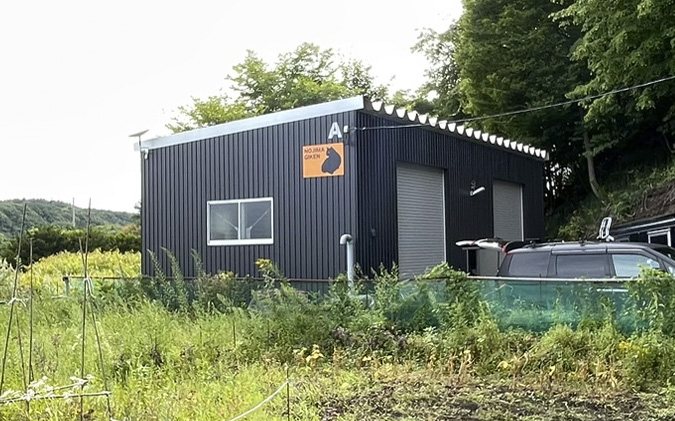 草地越しに見たガレージ工房の全景。切妻屋根と2連のシャッター